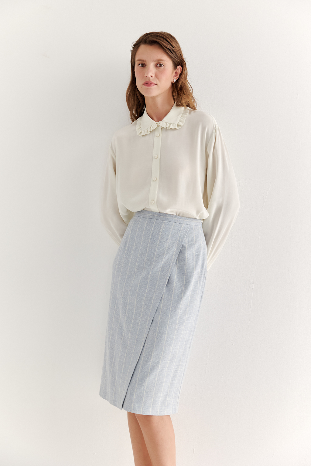 Прямая юбка с запахом выполнена из ткани, представляющей собой уникальную разработку бренда. Сочетание волокон хлопка, вискозы, полиэстера и эластана обеспечивает максимальный комфорт и практичность изделия. Нежный голубой цвет  эффектно подчёркнут светлой полоской в широком раппорте. Юбка идеально сочетается с жакетом архитектурного кроя из той же ткани, создавая завершённый формальный образ.