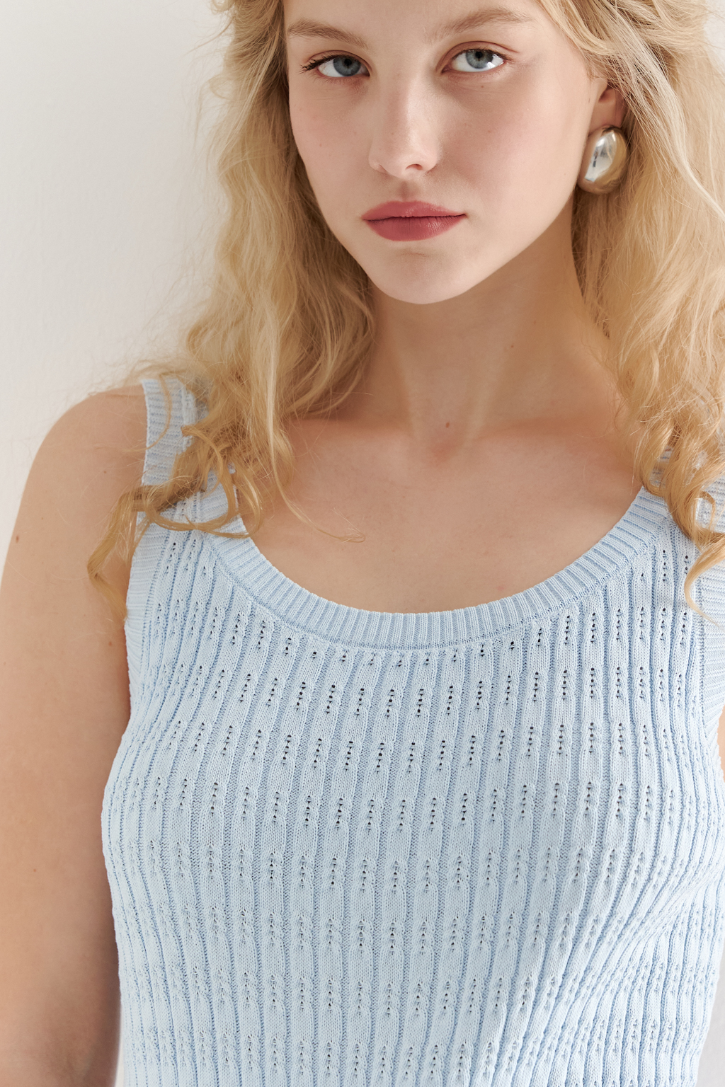 Фактурный топ-майка прилегающего силуэта из вискозной пряжи связана косами, проймы и горловина отделаны вязанными кантами. Цвет – голубой.