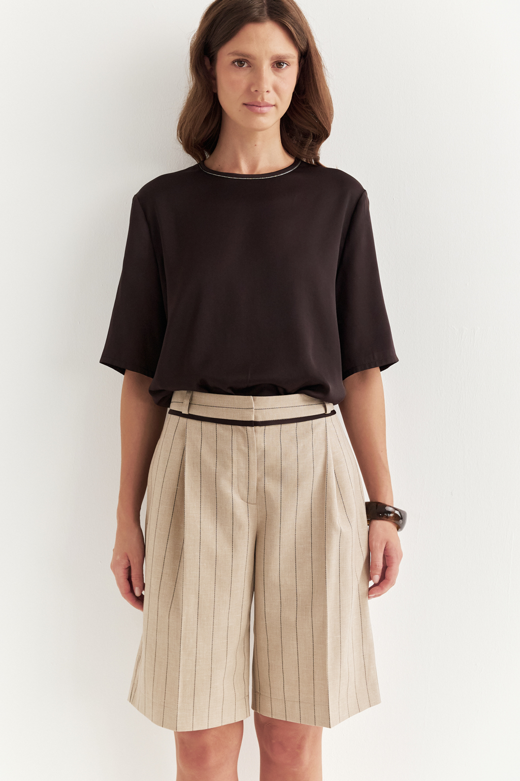 Элегантные шорты из костюмной ткани в полоску с деликатным меланжевым эффектом – безусловный фаворит сезона. Свободный, ниспадающий силуэт подчеркивает непринужденную элегантность и обеспечивает исключительный комфорт. Эти шорты великолепно дополняют жакеты, легкие трикотажные блузы или эффектные топы. Отголоски мужского кроя в дизайне проявляются в классической застежке-гульфике, поясе со шлевками, предусматривающем ношение ремня, и функциональных карманах. Аккуратный кант по линии пояса служит связующим звеном, объединяя шорты и идеально сочетающийся жакет в единый образ.