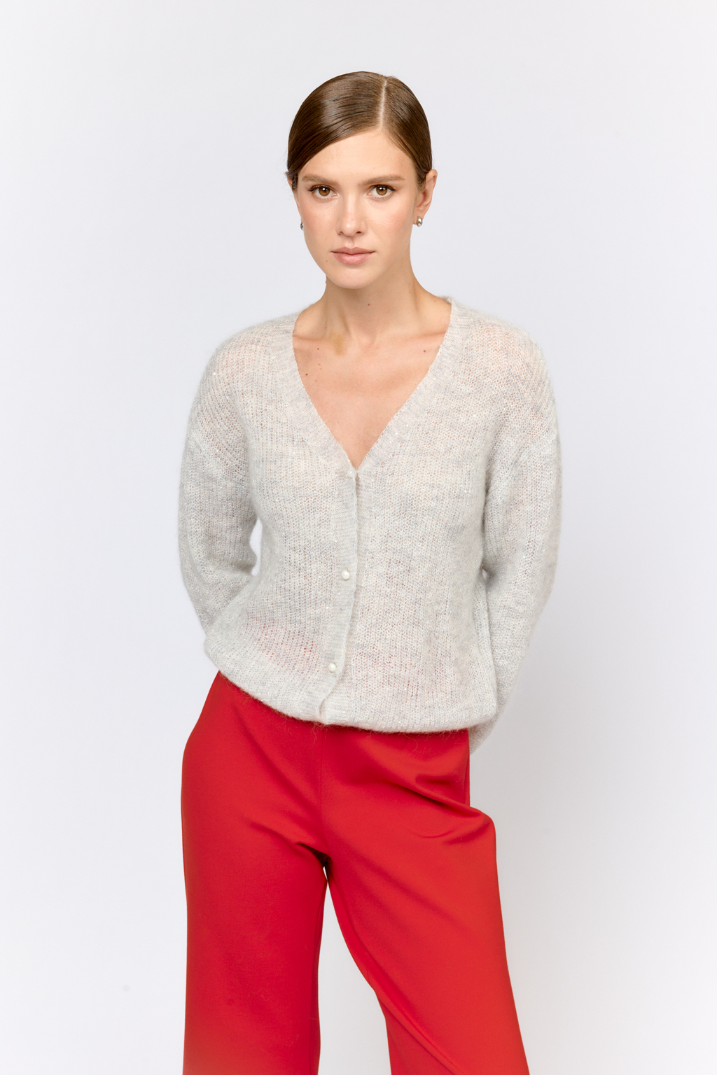 Кардиган с центральной застежкой на пуговицы, V-образной горловиной и длинным рукавом.  Модель свободного силуэта в жемчужно-сером  оттенке из воздушной пряжи с шерстью и мохером с деликатными мелкими пайетками, придающими легкое сияние. Кардиган очень теплый, несмотря но свою трендовую транспарентность и легкость, благодаря мохеру в составе. Шерсть так же обеспечивает естественную терморегуляцию и уют. Такой кардиган будет выигрышно смотреться в образах с  брюками и юбками из коллекции, а так же дополнит образы с платьями на бретелях или платьем-бандо.