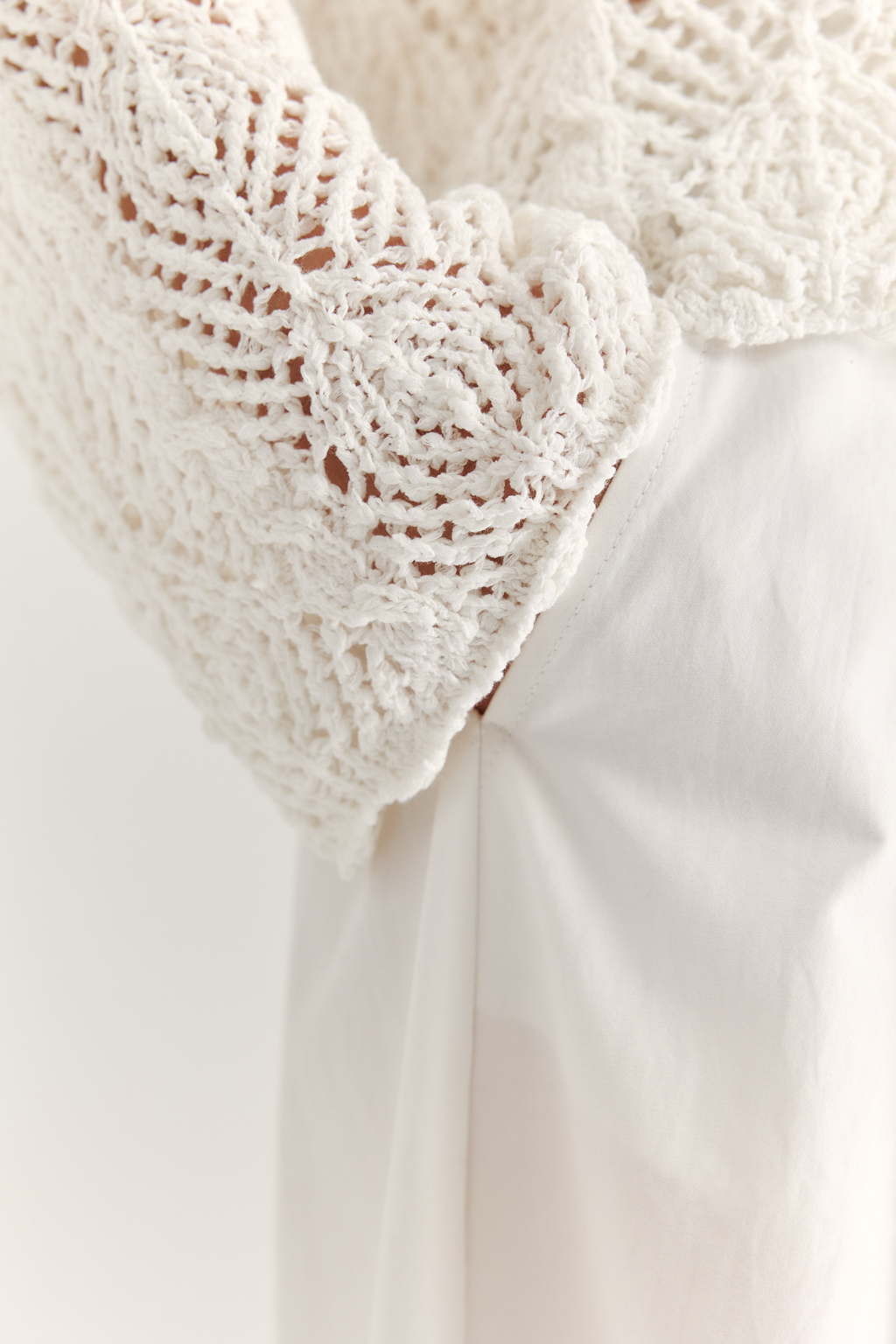 Белый вязаный кардиган оверсайз силуэта из хлопковой пряжи. Кардиган связан в сложной технике комбинирования сетки и ажурных ромбов. Рукав прямой удлиненный, V-образный вырез, борт отделан планкой, застежка по борту на 3 пуговицы, низ кардигана и рукав – сложные фестоны.