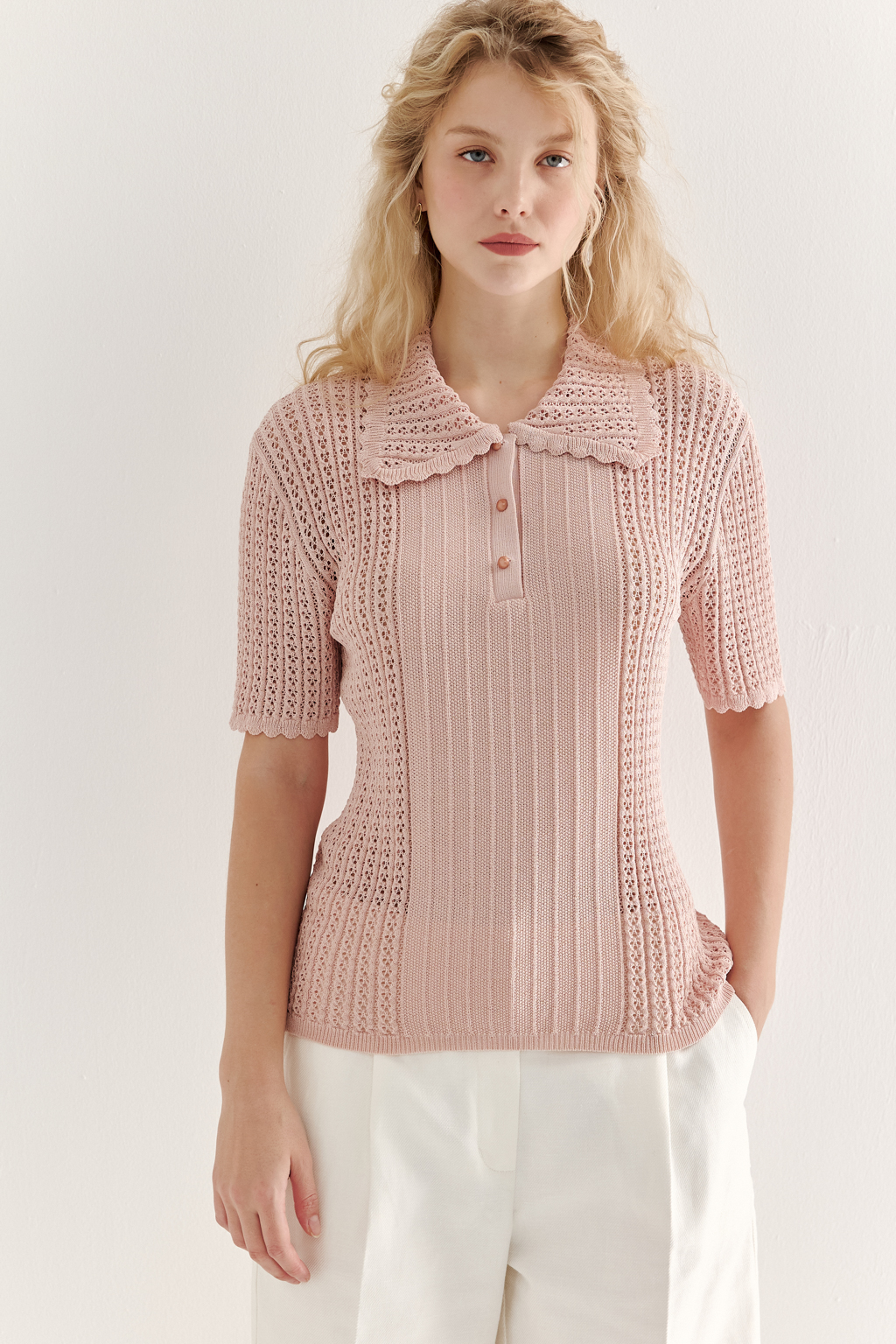 Джемпер-поло нежно-розового цвета полуприлегающего силуэта средней длины из вискозной пряжи, выполнен в комбинации полупрозрачной сетки и жаккарда, низ рукава и оторочка воротника - изящные фестоны. Рукав короткий, застежка на укороченной планке горловины на три пуговицы.