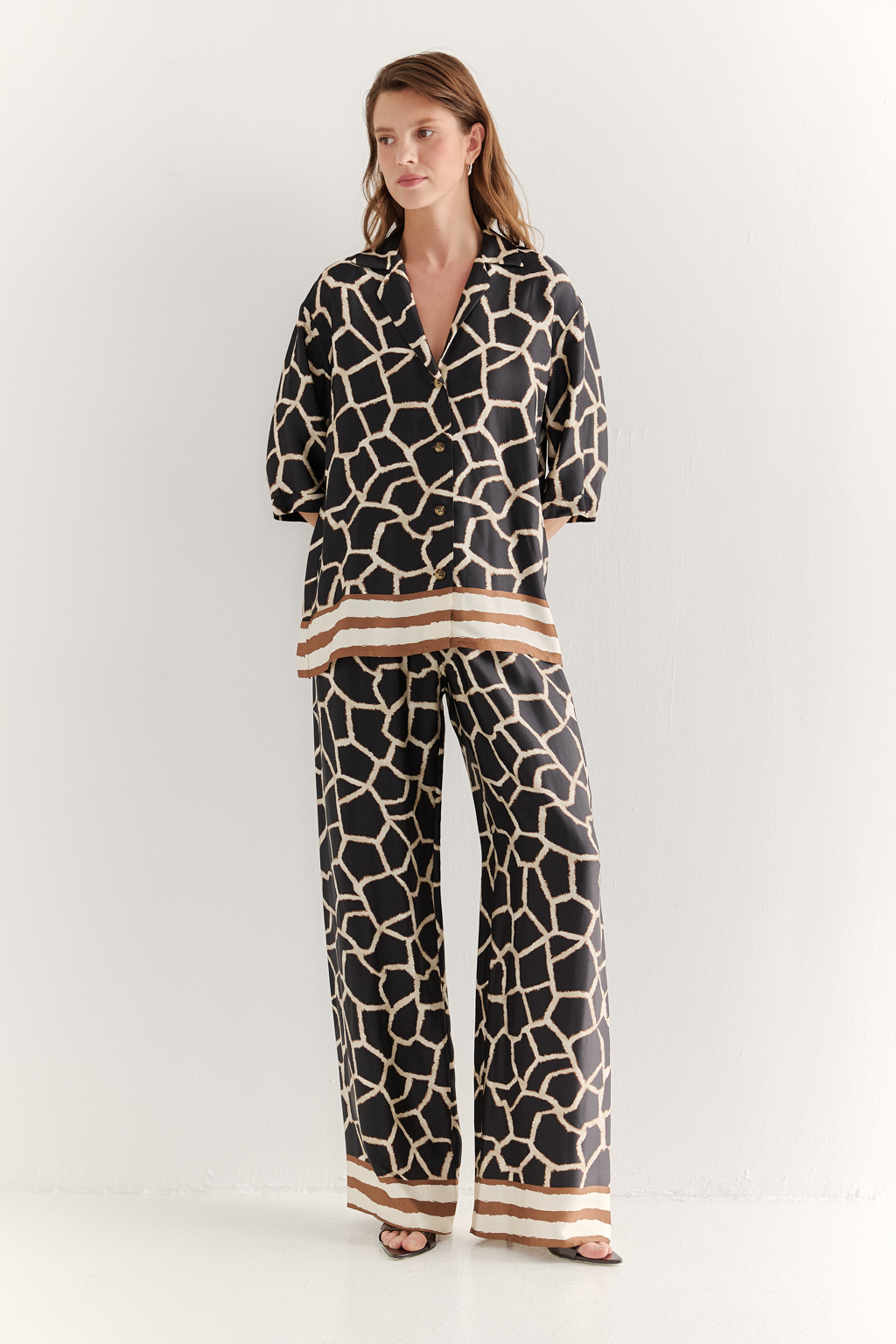 Блуза с коротким рукавом, выполненная из полированной вискозы с шелковистой текстурой, украшена эксклюзивным анималистическим принтом, разработанным дизайнерами бренда. Отложной воротник, застежка на пуговицы по переду и деликатные разрезы в боковых швах подчеркивают изысканный силуэт. Уникальный бордюр завершает принт по низу изделия, добавляя акцент. Блуза, сочетающая в себе непринужденный стиль и комфорт, идеально подходит в качестве второго слоя к пижамным брюкам из той же коллекции, создавая гармоничный и расслабленный образ.