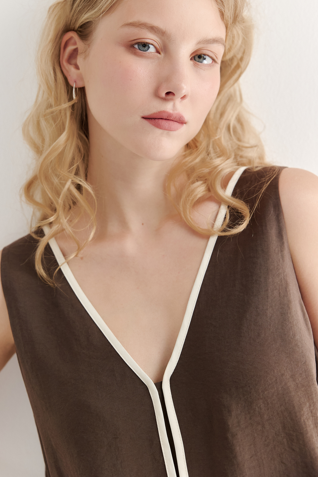 Блуза без рукавов, трапециевидного силуэта, выполнена из модала насыщенного шоколадно-коричневого оттенка и отделана контрастным кантом. Ткань обладает бархатистой текстурой, создающей так называемый "Peach эффект": благодаря специальной обработке на поверхности ткани образуется деликатный ворс, тактильно напоминающий кожицу персика. Горловина, центральный шов переда, боковые швы, а также шнуровка на спинке оформлены шелковистым кантом нежного молочного цвета. В боковых швах предусмотрены разрезы. Данная блуза прекрасно сочетается с элегантными брюками с лампасами из аналогичной ткани