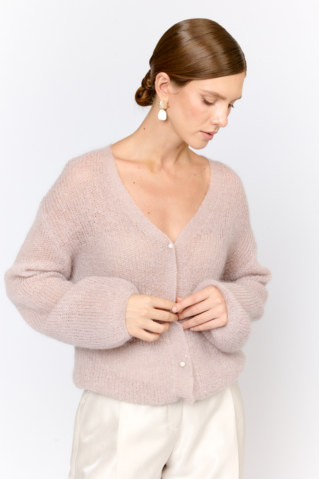 Кардиган с центральной застежкой на пуговицы, V-образной горловиной и длинным рукавом. Модель свободного силуэта в нежном пудровом оттенке из воздушной пряжи с шерстью и мохером с деликатными мелкими пайетками, придающими легкое сияние. Кардиган очень теплый, несмотря на свою трендовую транспарентность и легкость, благодаря мохеру в составе. Шерсть так же обеспечивает естественную терморегуляцию и уют. Такой кардиган будет выигрышно смотреться в образах с брюками и юбками из коллекции, а так же дополнит образы с платьями на бретелях или платьем-бандо.