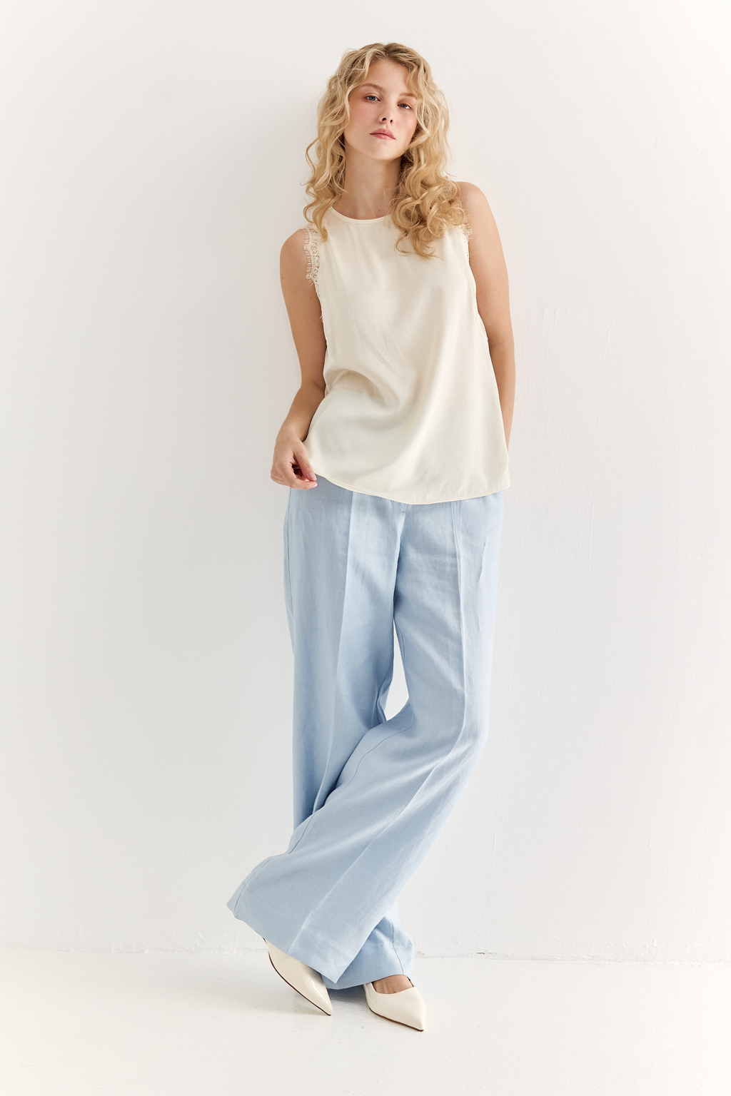 Блуза без рукавов из струящегося сатина в оттенке сливочное масло. Круглая горловина обработана кантом, на спинке воздушная петля с застежкой на пуговицу, по проймам настрочена тесьма из гипюра в тон основной ткани.