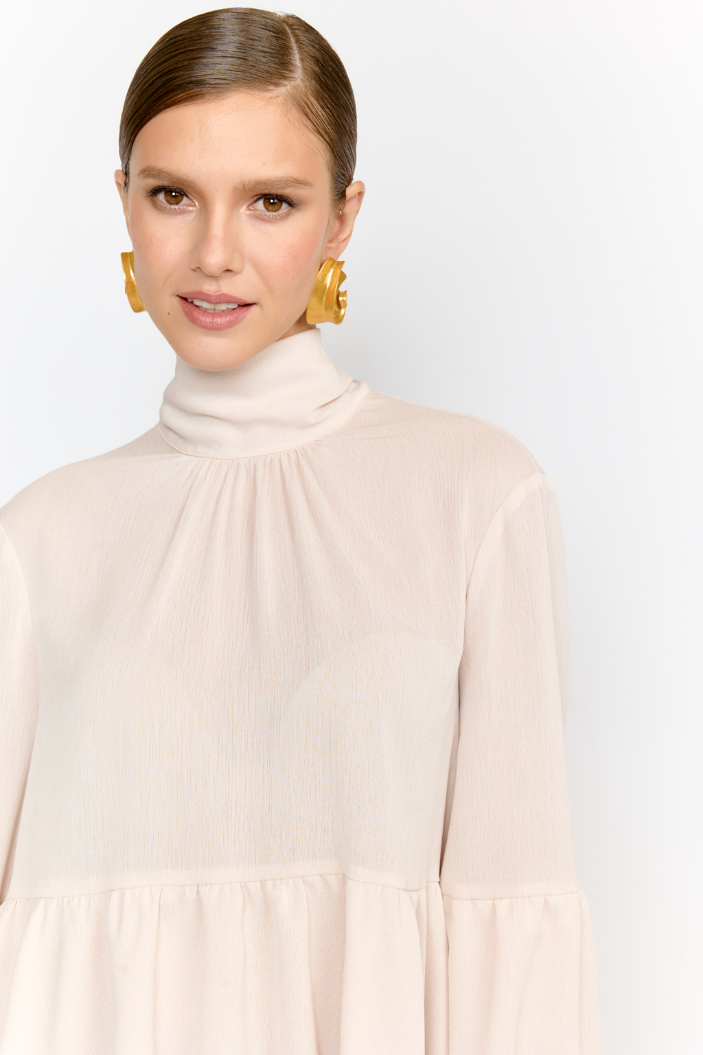 Блуза свободного кроя с легким расширением к низу с воланами и воротником-стойкой, переходящим в ленты, которые можно завязать в бант либо просто перекинуть через плечи. Выполнена из легкой полупрозрачной ткани. Крэш-шифон -легкий, дышащий материал, создающий эффект невесомости. Полиэстеровые волокна в составе обеспечивают   неприхотливость в уходе и устойчивость к механическим повреждениям. Нежный цвет экрю позволяет легко вписать блузу в гардероб, для создания как праздничных образов, так и повседневных.