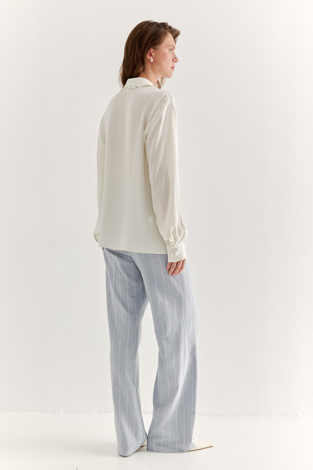 Блуза-батник в нежном оттенке сливочное масло станет изысканным дополнением к жакету, брюкам или верхней одежде, позволяя создавать актуальные многослойные образы. Изготовленная из вискозной ткани, она обладает превосходными тактильными качествами и напоминает дорогой шелковый креп. Классическая блузка свободного кроя с отложным воротником и стойкой, украшенной узким рюшем, имеет планку для застежки и втачной прямой рукав с манжетой на пуговицах.