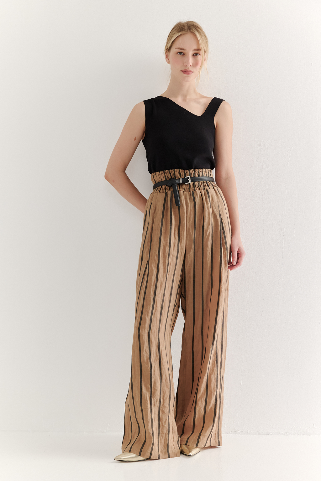 Брюки прямого кроя с широким поясом, собранным в сборку, сшиты из платьевой ткани в тонкую полоску. Состав ткани - сочетание волокон крапивы и хлопка, обработанных с эффектом растительного окрашивания (natural dye). Темная полоска на бежевом фоне идеально гармонирует с силуэтом широких брюк, подчеркивая их элегантную простоту. Пояс брюк широкий, собран на три ряда кулисок с резинками, что позволяет регулировать его высоту посадки относительно линии талии. Ткань обладает свойством создавать естественный крэш-эффект, придающий изделию легкую текстурную небрежность и объем, при этом брюки не требуют сложного ухода.