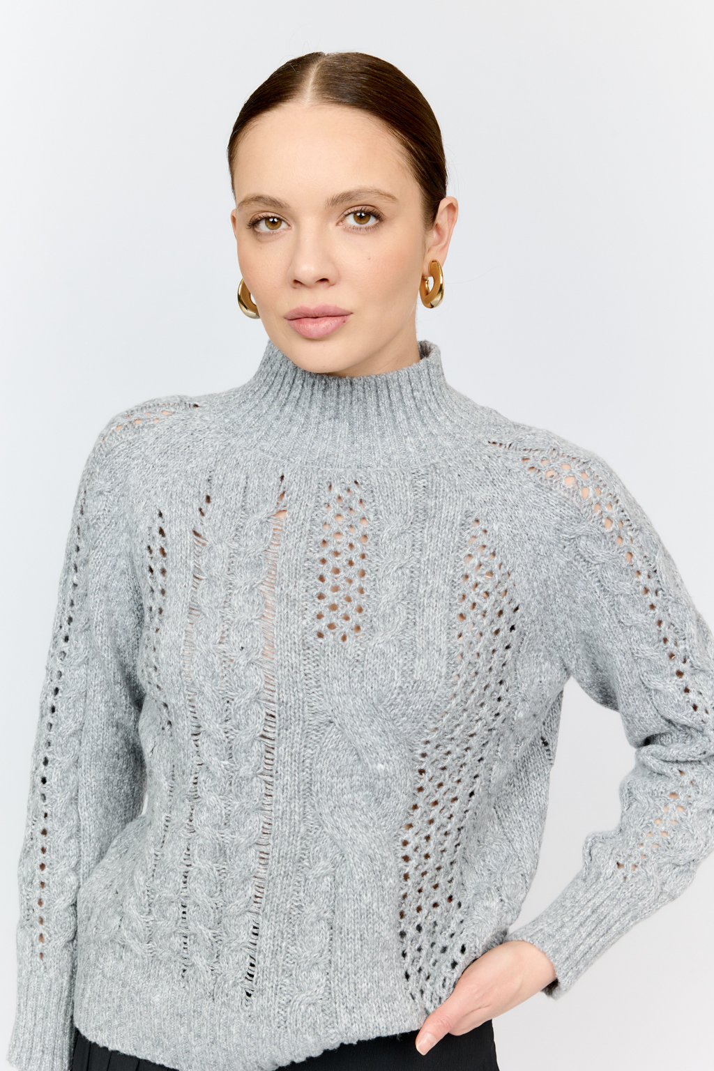 Свитер серого цвета из мягкой пряжи фигурной вязки с ассиметричными косами, с высокой горловиной и длинным рукавом реглан отлично стилизуется с денимом и обувью на плоском ходу.