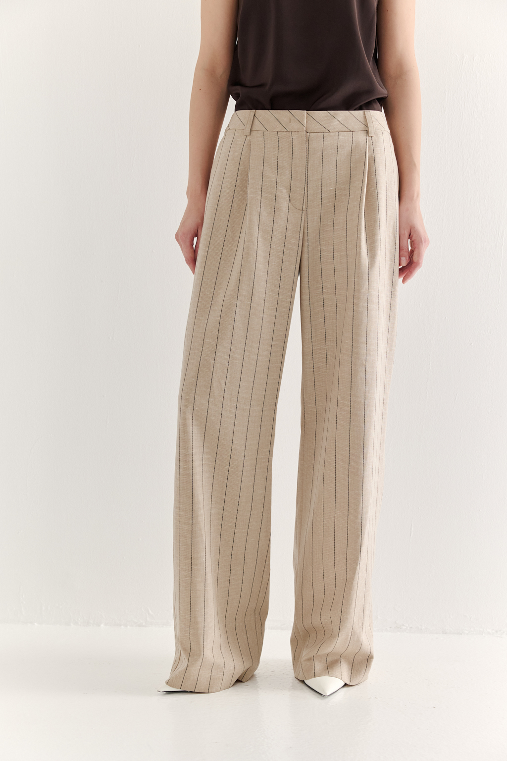 Брюки классического силуэта, прямые и широкие по всей длине, выполнены из костюмной ткани в изысканную полоску с деликатным меланжевым эффектом. В состав ткани входят волокна лиоцелла, льна, вискозы и спандекса, что гарантирует не только исключительный комфорт, но и повышенную износостойкость изделия. Дизайн модели вдохновлен элементами традиционного мужского кроя, включая застежку-гульфик, пояс со шлевками и практичные карманы. Передние половинки брюк оформлены элегантными складками-защипами у верхнего среза. Данная модель идеально дополнит сложный, многослойный ансамбль с пиджаком из аналогичной ткани, а также станет ключевым акцентом в сочетании с лаконичным трикотажным топом.