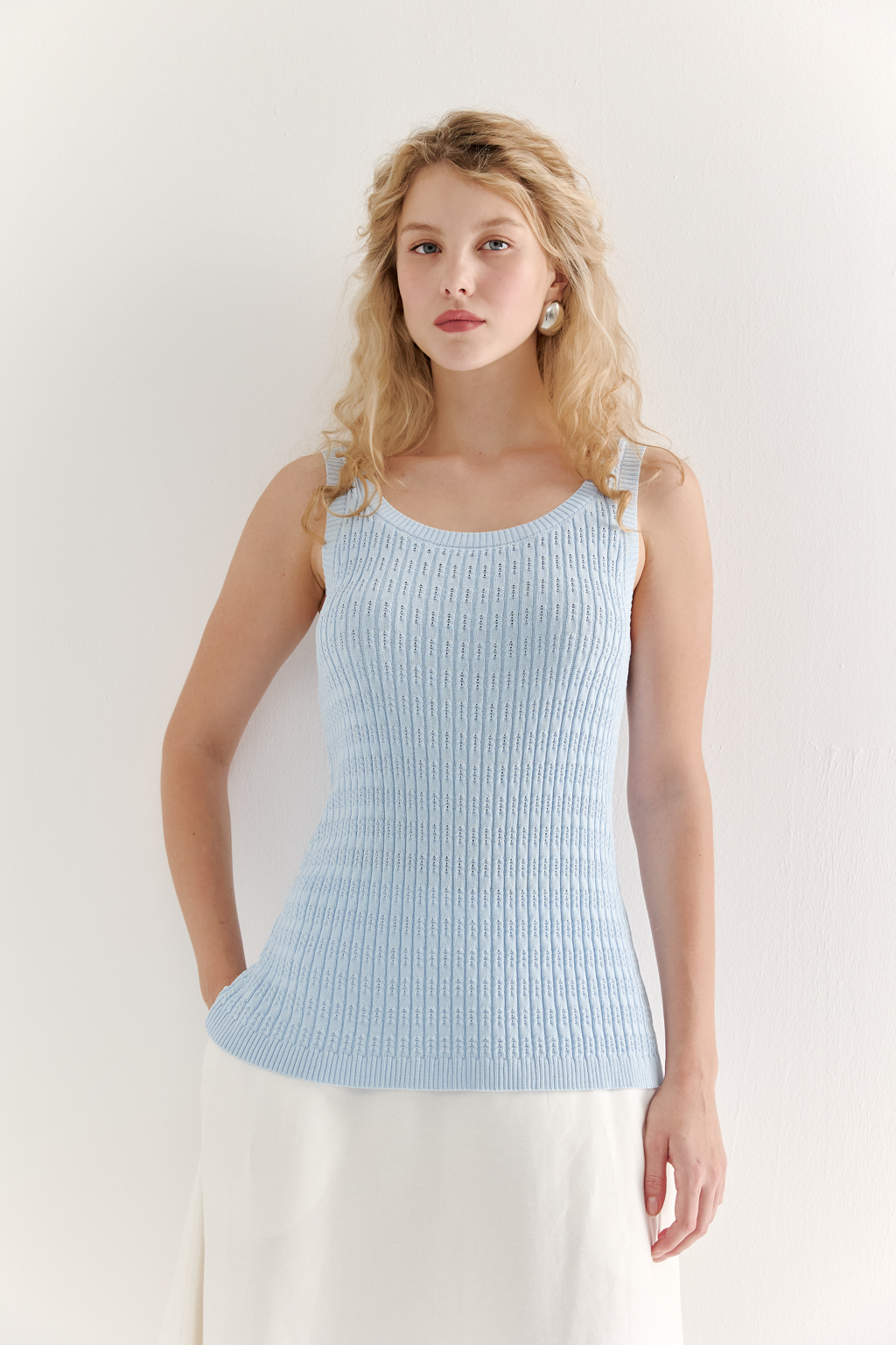 Фактурный топ-майка прилегающего силуэта из вискозной пряжи связана косами, проймы и горловина отделаны вязанными кантами. Цвет – голубой.