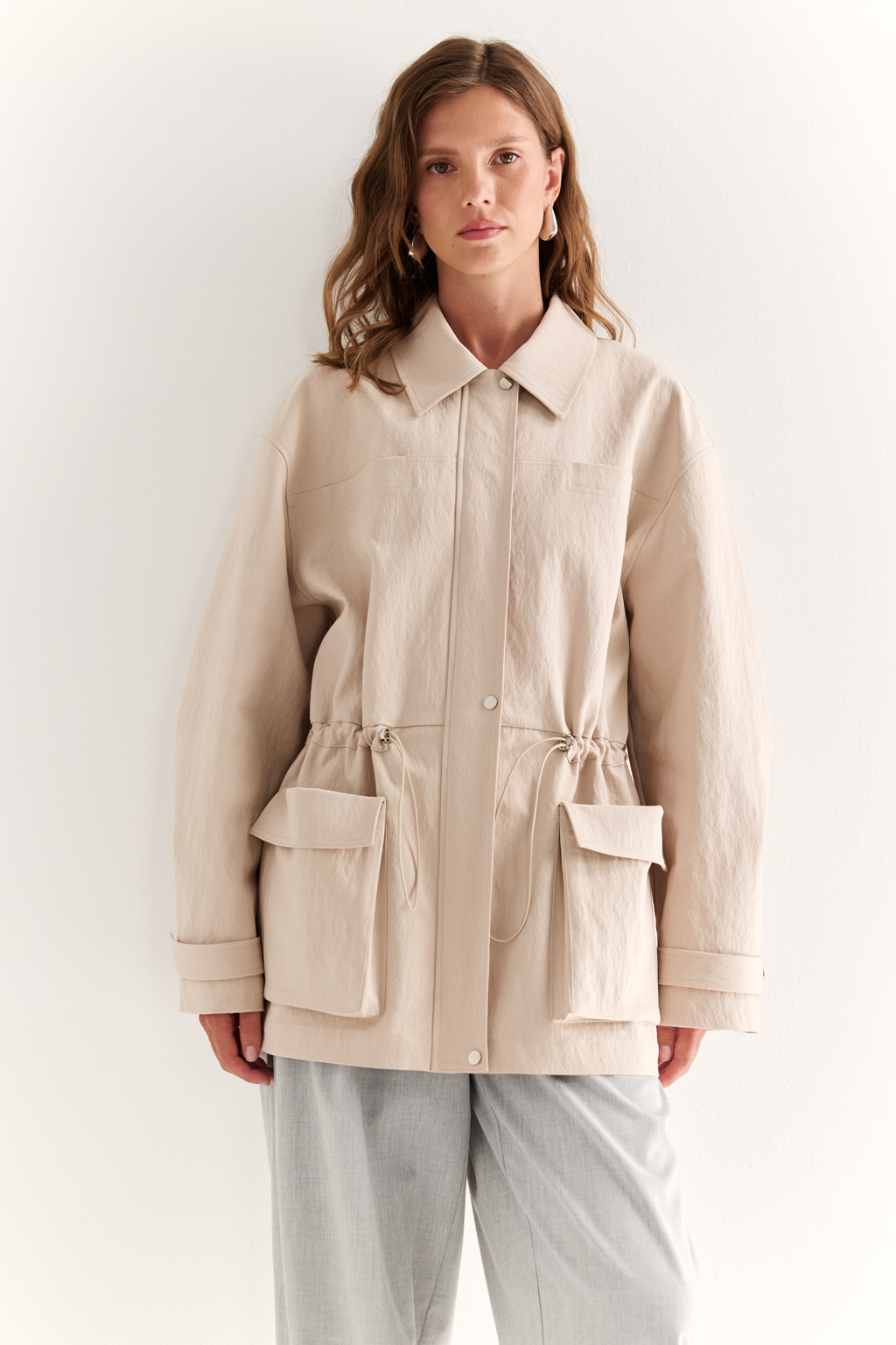Куртка прямого силуэта длиной до бедер и с кулисой по талии. Воротник рубашечный, застежка под планкой. По полочке накладные карманы-портфели.