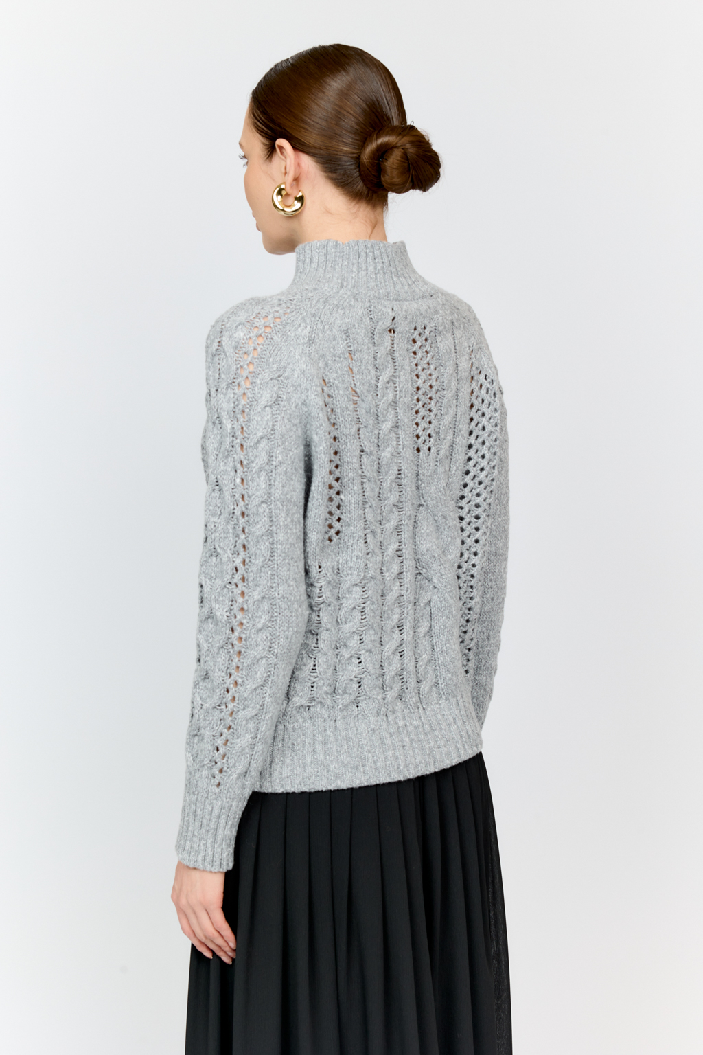 Свитер серого цвета из мягкой пряжи фигурной вязки с ассиметричными косами, с высокой горловиной и длинным рукавом реглан отлично стилизуется с денимом и обувью на плоском ходу.