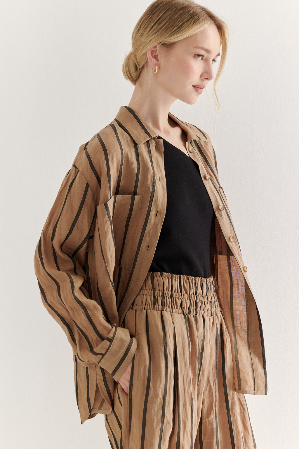 Блуза-рубашка свободного кроя изготовлена сшиты из ткани в темную полоску на песочном фоне. Ткань сочетает в себе волокна крапивы и хлопка, прошедшие обработку с использованием натуральных красителей (natural dye). Дизайн, вдохновлённый классической мужской рубашкой, включает в себя воротник-стойку, планку с застёжкой и длинные рукава с манжетами. Свободный расслабленный стиль рубашки идеально рифмуется с комфортными брюками из этой же ткани и компактными трикотажными джемперами и топами. Яркое решение образа создает комфортный и запоминающийся образ