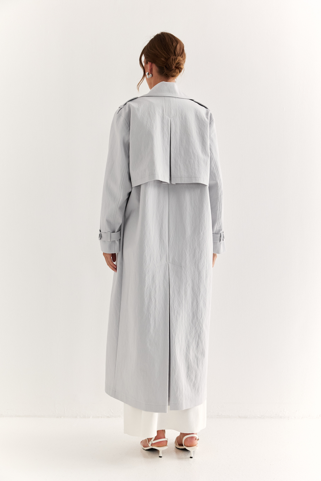 Плащ двубортный прямого силуэта длиной макси с расширенной линией плеча и отлётными кокетками по полочке и спинке. Приталивается завязывающимся поясом.