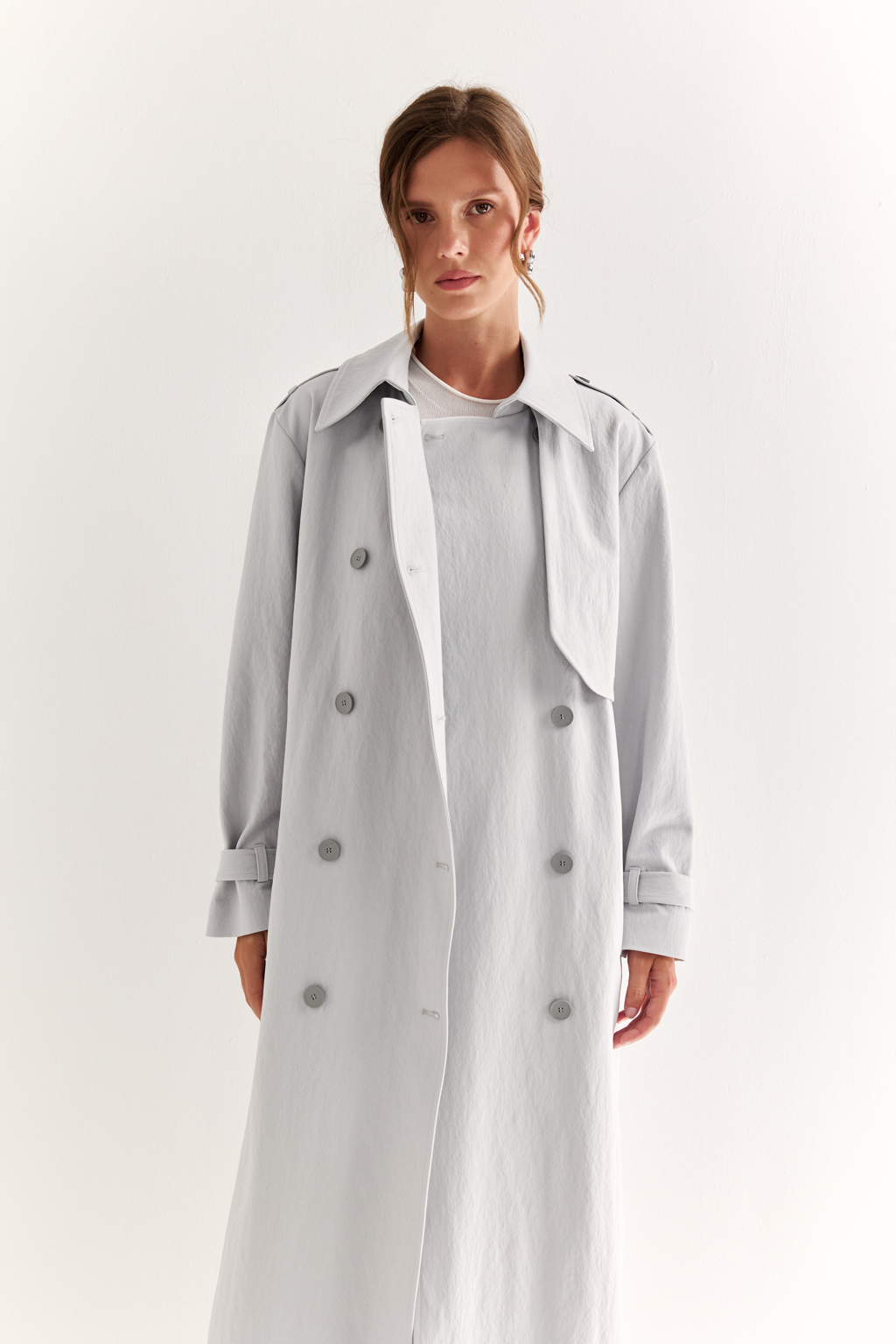 Плащ двубортный прямого силуэта длиной макси с расширенной линией плеча и отлётными кокетками по полочке и спинке. Приталивается завязывающимся поясом.
