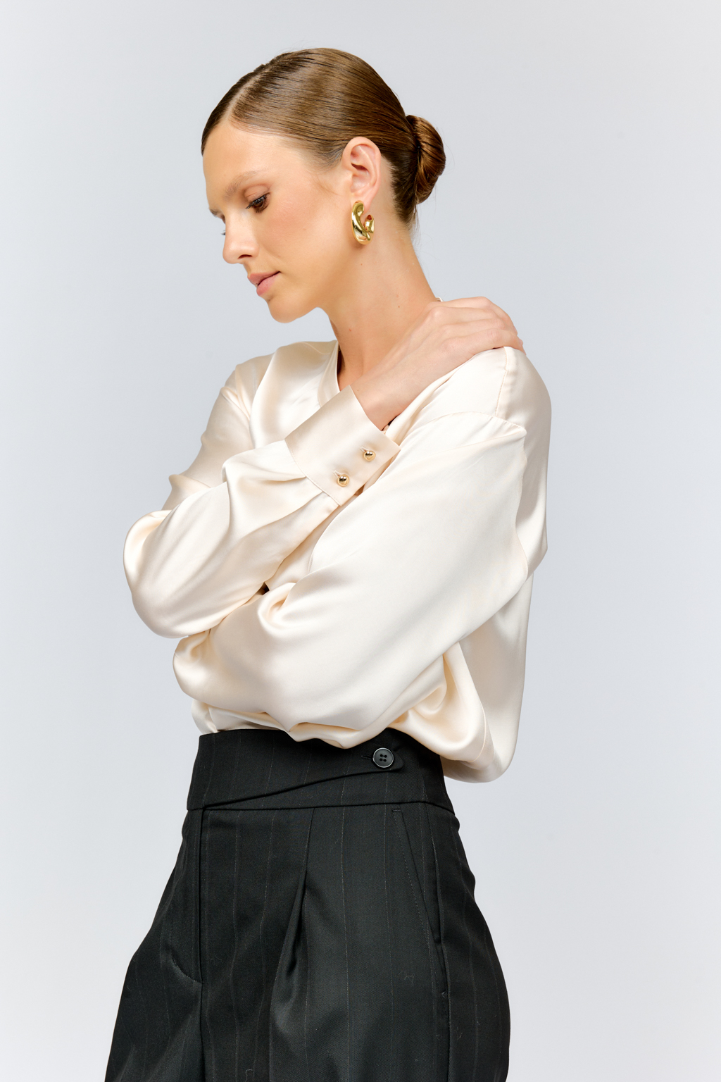 Блуза свободного кроя из шелковистой вискозы с интересной деталью в виде складки на горловине с застежкой на декоративную золотую пуговицу. Изделие придаст стильный акцент к любому образу.