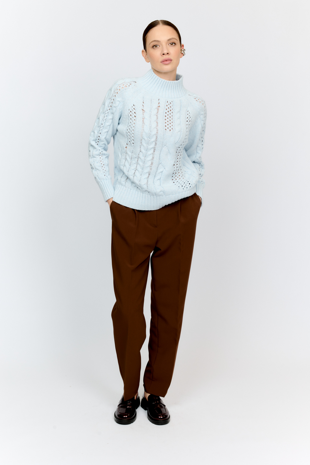 Свитер голубого цвета из мягкой пряжи фигурной вязки с ассиметричными косами, с высокой горловиной и длинным рукавом реглан отлично стилизуется с денимом и обувью на плоском ходу.