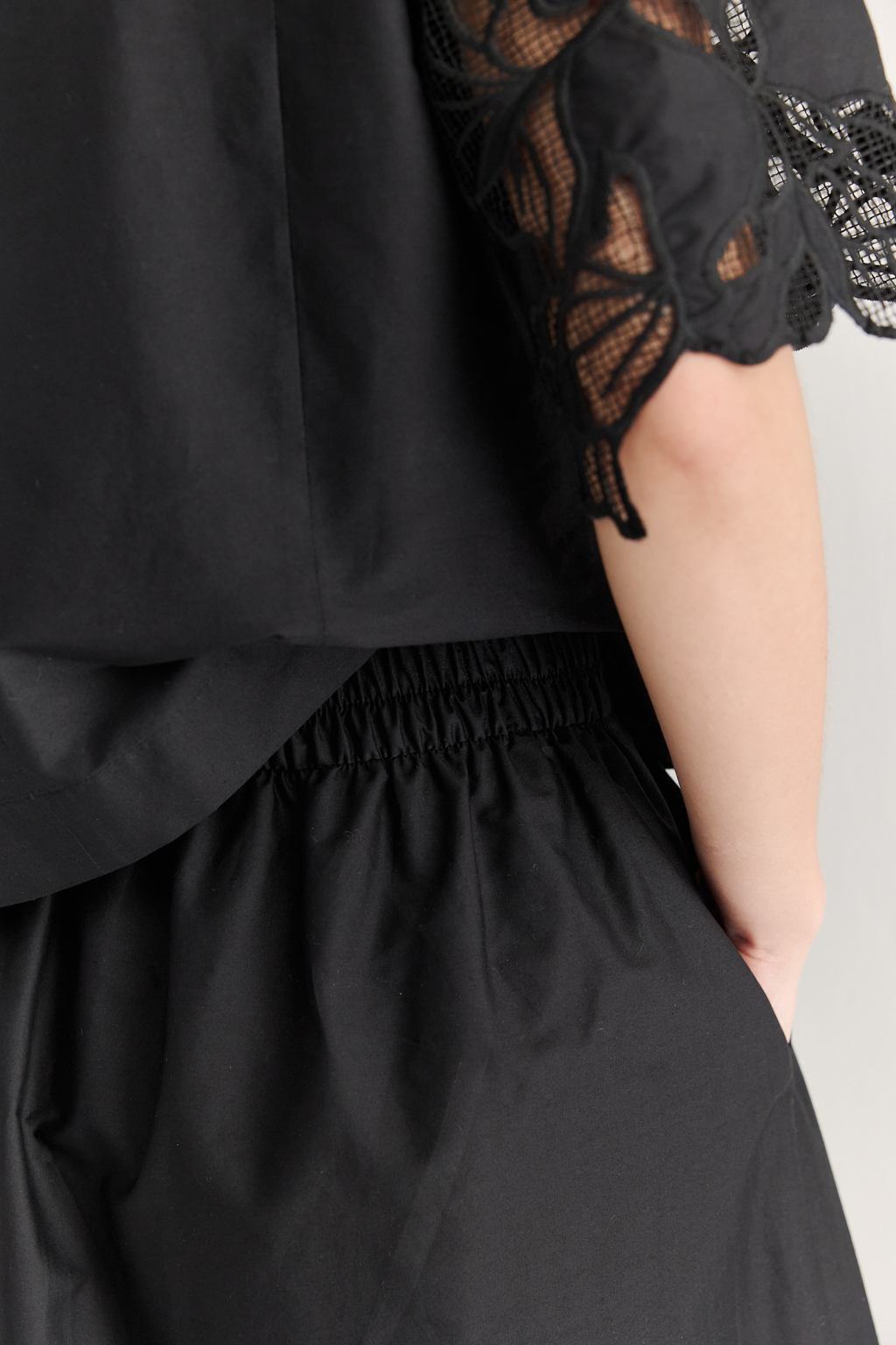 Блуза-кроп выполненная из хлопкового полотна, декорирована нежным шитьем-решелье черного цвета. Укороченный силуэт блузы дополнен широкой подгибкой по низу и элегантными разрезами в боковых швах. Горловина оформлена в виде лодочки, визуально удлиняя шею. Широкие рукава имеют сборку по окату и украшены шитьем по низу, что придает образу легкости и женственности. Молния, расположенная в среднем шве спинки, обеспечивает комфорт и удобство при носке. Идеально подойдет к юбке с шитьем-решелье белого цвета.