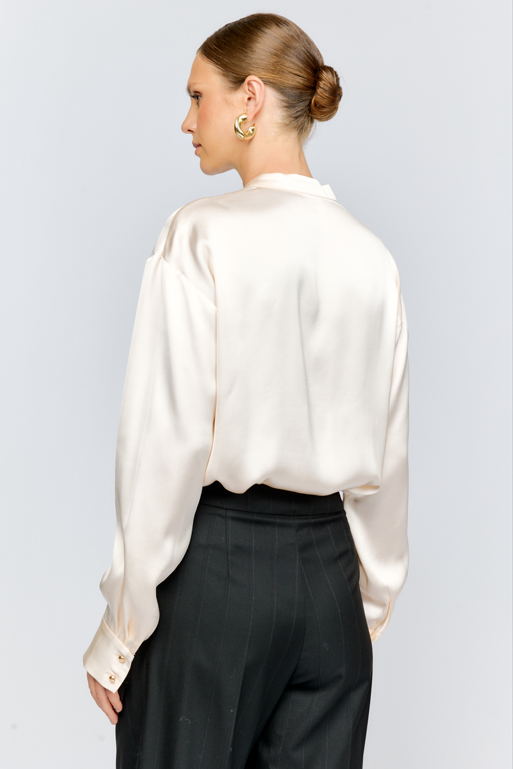 Блуза свободного кроя из шелковистой вискозы с интересной деталью в виде складки на горловине с застежкой на декоративную золотую пуговицу. Изделие придаст стильный акцент к любому образу.
