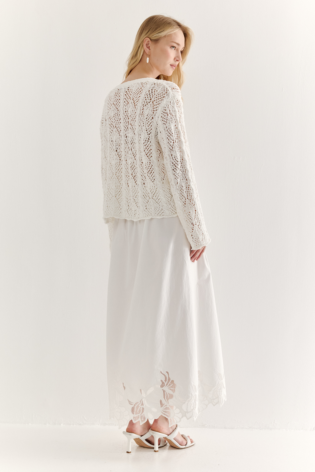 Белый вязаный кардиган оверсайз силуэта из хлопковой пряжи. Кардиган связан в сложной технике комбинирования сетки и ажурных ромбов. Рукав прямой удлиненный, V-образный вырез, борт отделан планкой, застежка по борту на 3 пуговицы, низ кардигана и рукав – сложные фестоны.