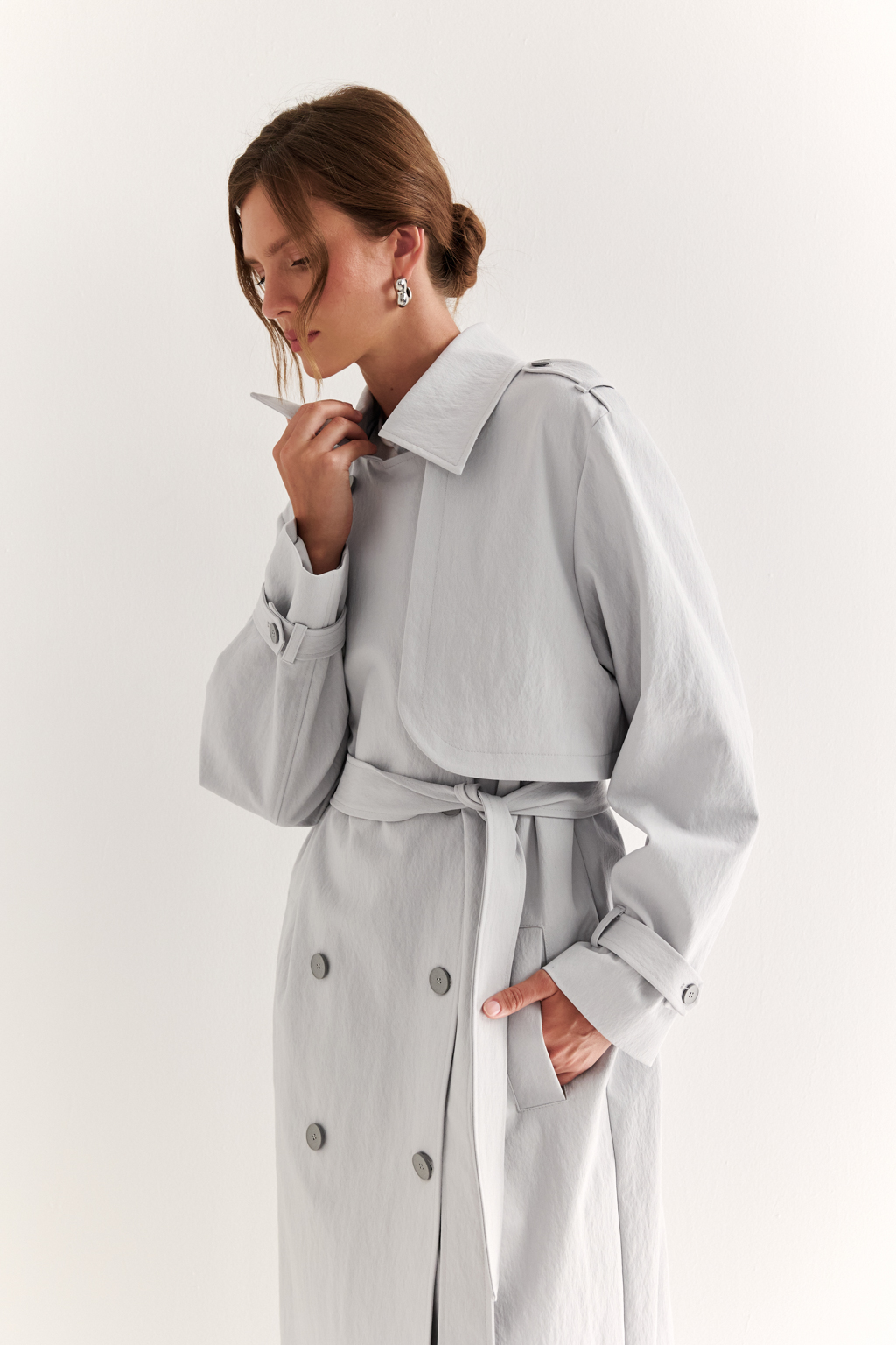 Плащ двубортный прямого силуэта длиной макси с расширенной линией плеча и отлётными кокетками по полочке и спинке. Приталивается завязывающимся поясом.