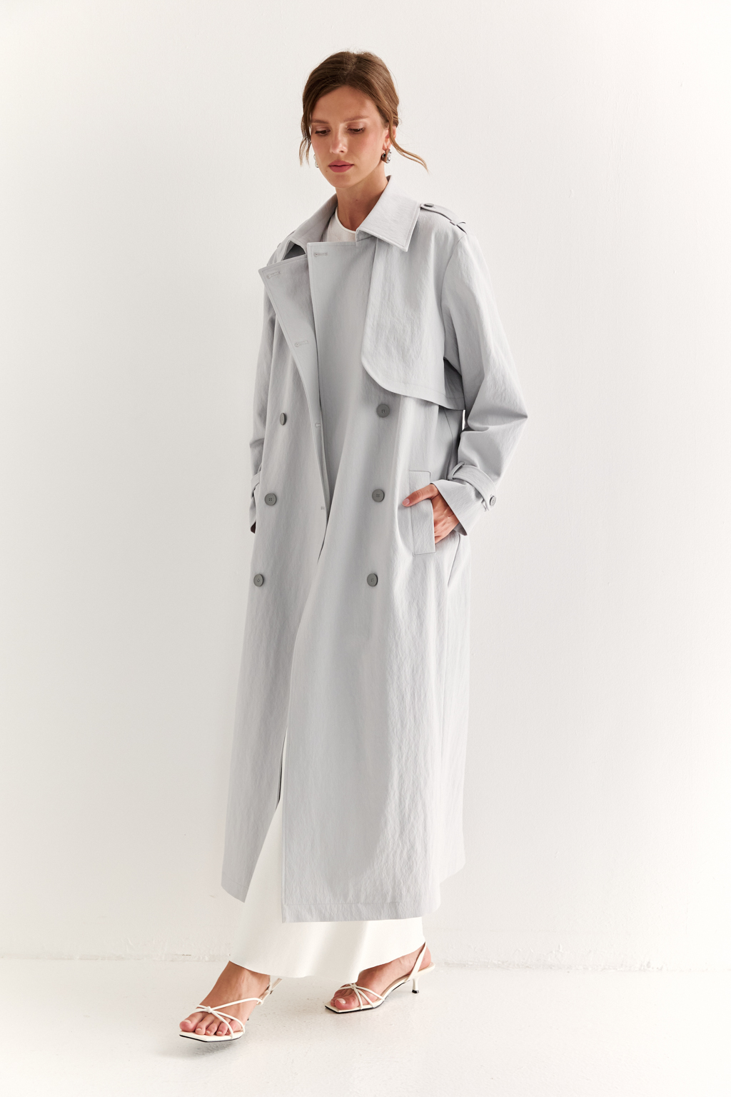 Плащ двубортный прямого силуэта длиной макси с расширенной линией плеча и отлётными кокетками по полочке и спинке. Приталивается завязывающимся поясом.