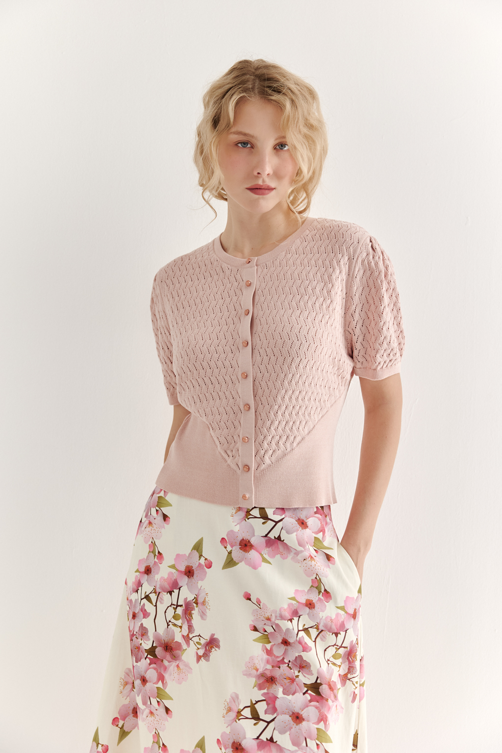 Джемпер нежно-розового цвета, связанный из тонкой тактильной пряжи, в составе которой вискоза и нейлон. В дизайне джемпера применен принцип контраста фактур, в данном случае – полупрозрачного ажура и ластика. Круглая горловина и планка с застежкой на 9 пуговиц-жемчужин, рукав длиной одна вторая.