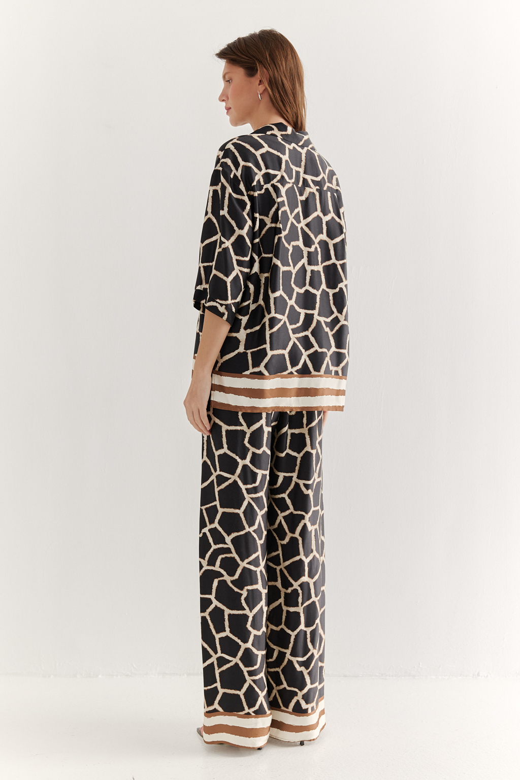 Блуза с коротким рукавом, выполненная из полированной вискозы с шелковистой текстурой, украшена эксклюзивным анималистическим принтом, разработанным дизайнерами бренда. Отложной воротник, застежка на пуговицы по переду и деликатные разрезы в боковых швах подчеркивают изысканный силуэт. Уникальный бордюр завершает принт по низу изделия, добавляя акцент. Блуза, сочетающая в себе непринужденный стиль и комфорт, идеально подходит в качестве второго слоя к пижамным брюкам из той же коллекции, создавая гармоничный и расслабленный образ.