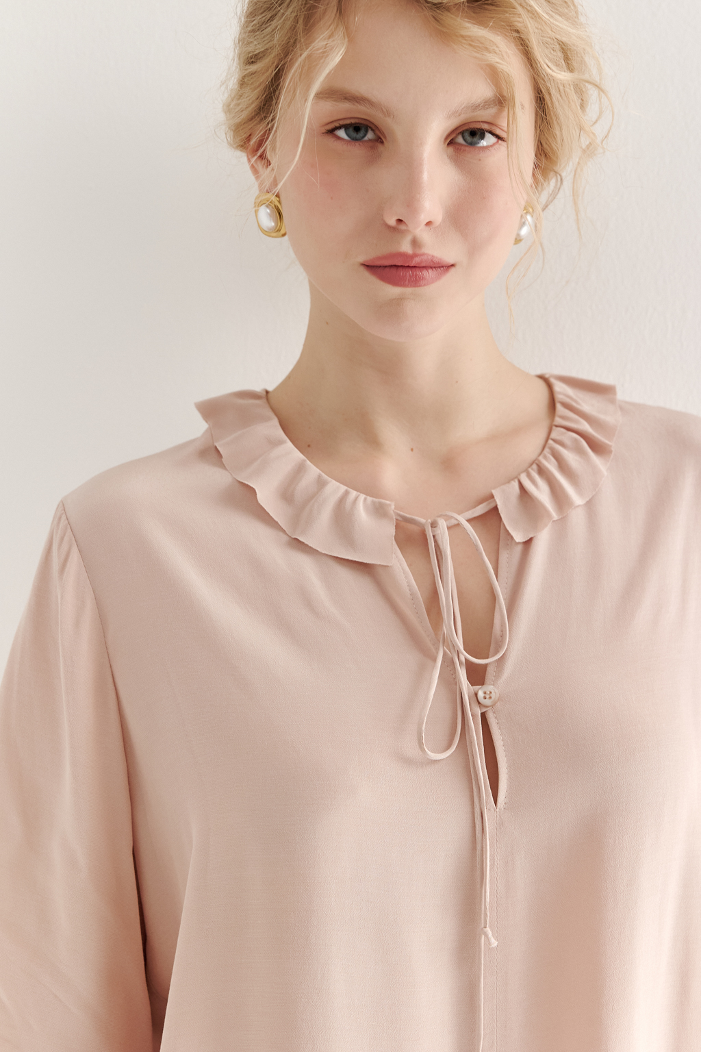 Эта романтичная блуза выполнена из вискозного крепа в нежном пудрово-розовом оттенке. Горловина и рукава украшены изящными рюшами, добавляющими образу легкости и утонченности. Оригинальный разрез спереди кокетливо завязывается на тонкий шнур-рулик и фиксируется воздушной петлей на пуговицу. Прямой силуэт и рукава длиной одна вторая обеспечивают комфорт и свободу движений. Эта блуза — идеальный выбор для создания непринужденных, но элегантных городских образов.