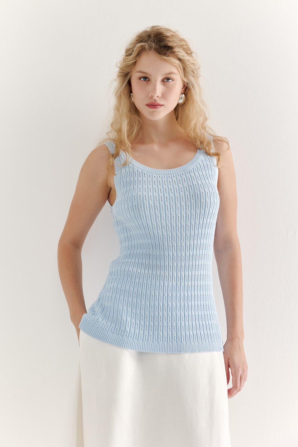 Фактурный топ-майка прилегающего силуэта из вискозной пряжи связана косами, проймы и горловина отделаны вязанными кантами. Цвет – голубой.