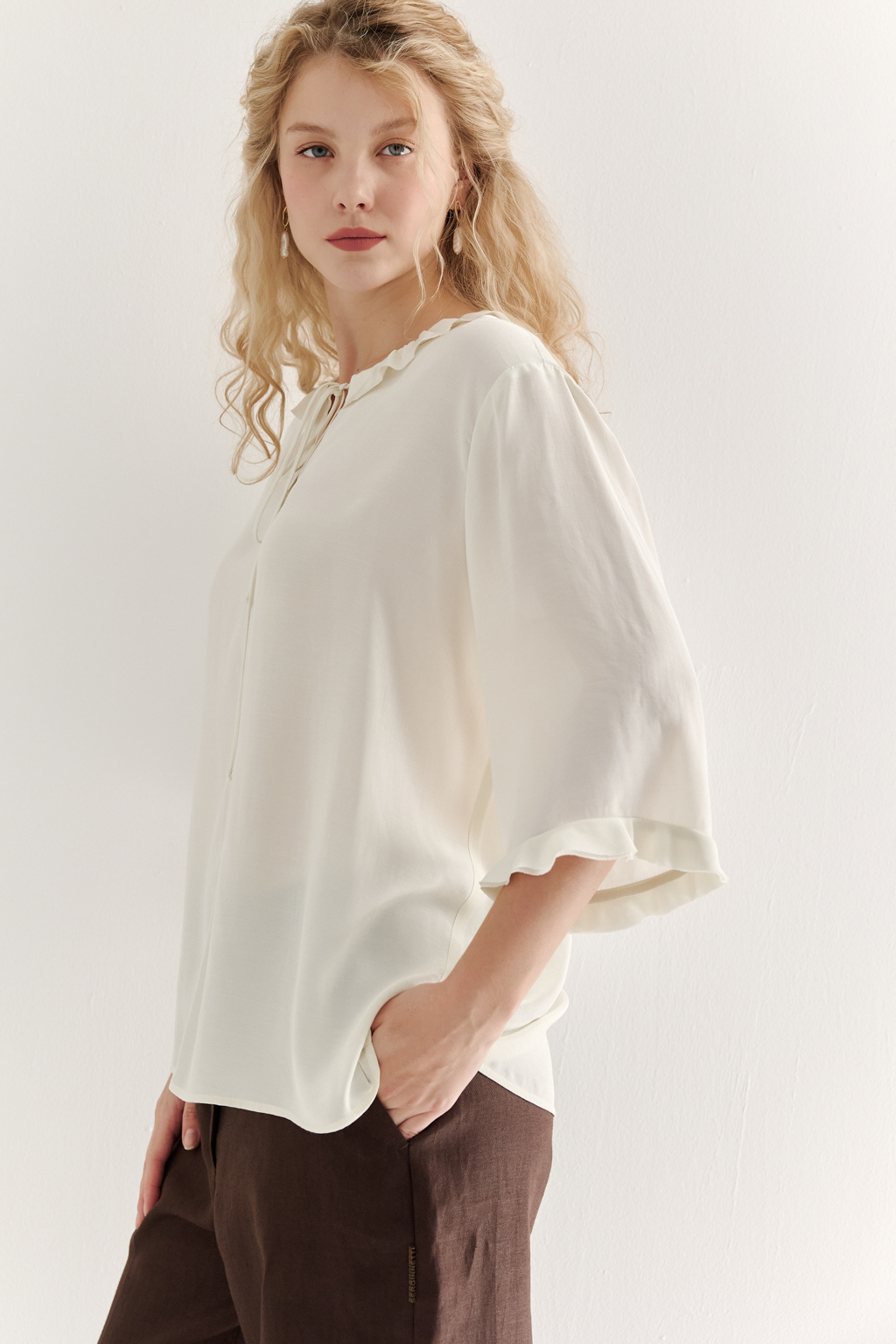Эта романтичная блуза выполнена из вискозного крепа в нежном оттенке словочное масло. Горловина и рукава украшены изящными рюшами, добавляющими образу легкости и утонченности. Оригинальный разрез спереди кокетливо завязывается на тонкий шнур-рулик и фиксируется воздушной петлей на пуговицу. Прямой силуэт и рукава длиной одна вторая обеспечивают комфорт и свободу движений. Эта блуза — идеальный выбор для создания непринужденных, но элегантных городских образов.