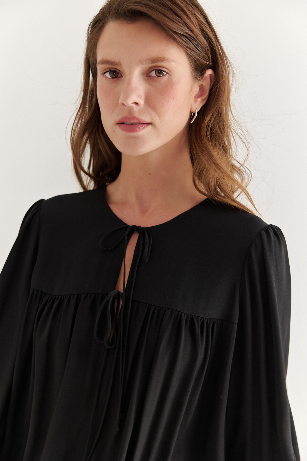 Платье, из струящейся креповой вискозы в черном цвете, представляет собой воплощение модных тенденций, умело играя с объемами с акцентом на заниженную линию талии. Это короткое, воздушное и исполненное романтики платье, сознательно избегающее вычурных деталей, является идеальным решением для создания актуального летнего городского образа. Объем платья образуется благодаря изящным сборкам, расположенным по кокеткам переда и спинки. Отрезная юбка, расширяющаяся к низу, украшена деликатной декоративной строчкой-вышивкой в виде фестонов. Линия отреза юбки оформлена эластичной тесьмой-стрейч, что дает возможность регулировать длину. Платье гармонично сочетается с рубашками или жакетами, предоставляя свободу для экспериментов со стилем. При желании можно усложнить образ образа с помощью леггинсов и также подчеркнуть талию элегантным кожаным ремнем.