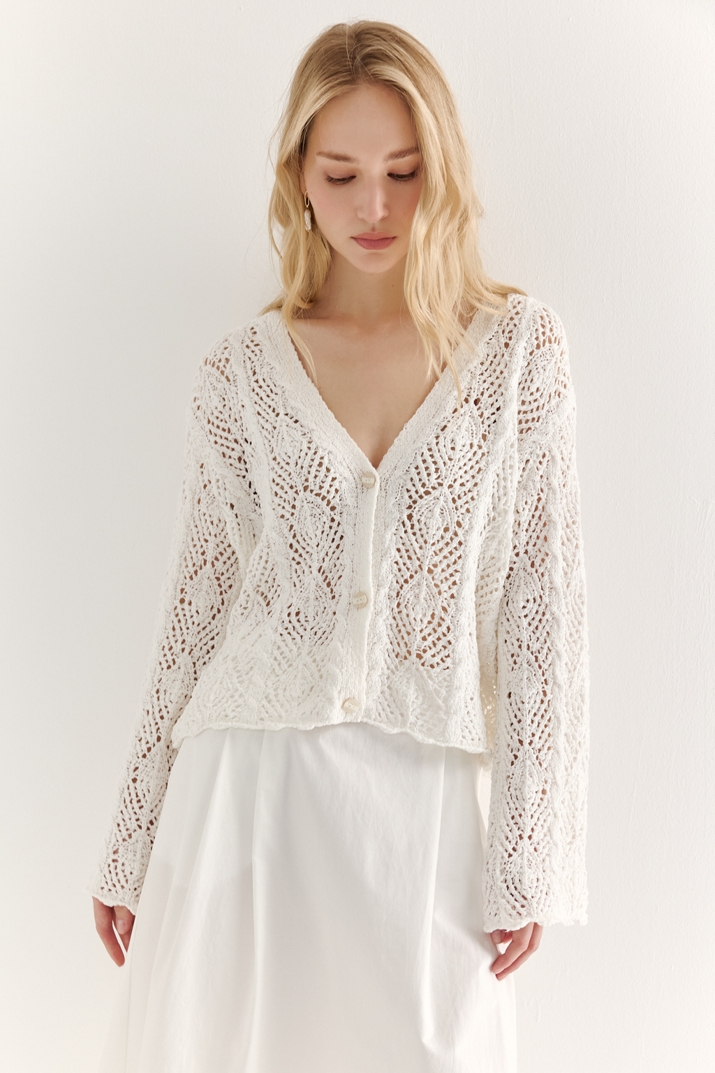 Белый вязаный кардиган оверсайз силуэта из хлопковой пряжи. Кардиган связан в сложной технике комбинирования сетки и ажурных ромбов. Рукав прямой удлиненный, V-образный вырез, борт отделан планкой, застежка по борту на 3 пуговицы, низ кардигана и рукав – сложные фестоны.