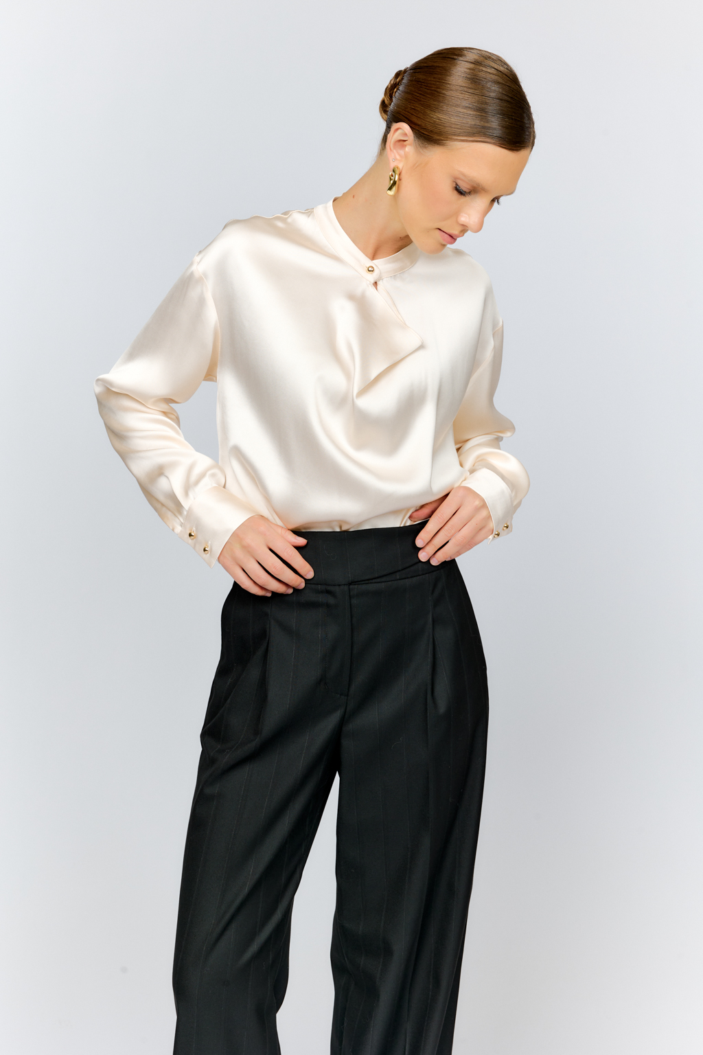 Блуза свободного кроя из шелковистой вискозы с интересной деталью в виде складки на горловине с застежкой на декоративную золотую пуговицу. Изделие придаст стильный акцент к любому образу.