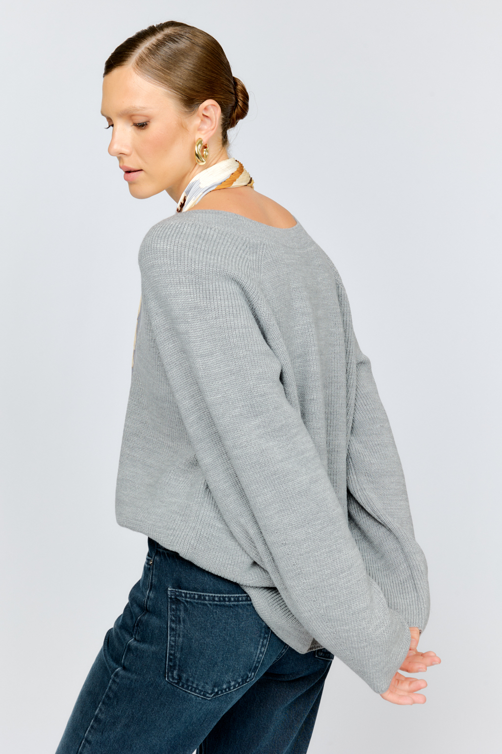 Трикотажный джемпер серого цвета свободного силуэта с V-образным вырезом горловины и рукавами реглан из шерстяной смесовой пряжи станет центром комфортных осенних образов.