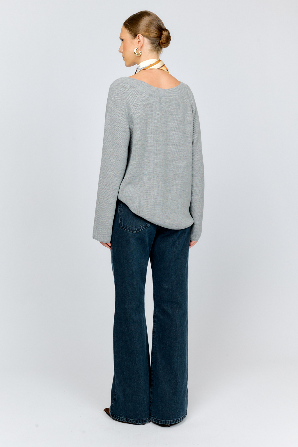 Трикотажный джемпер серого цвета свободного силуэта с V-образным вырезом горловины и рукавами реглан из шерстяной смесовой пряжи станет центром комфортных осенних образов.