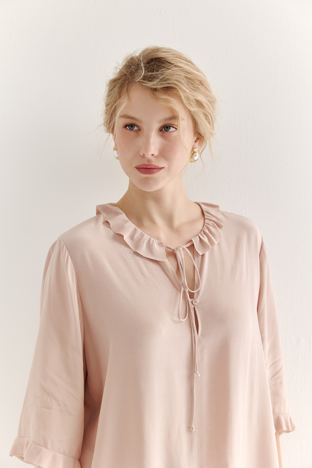 Эта романтичная блуза выполнена из вискозного крепа в нежном пудрово-розовом оттенке. Горловина и рукава украшены изящными рюшами, добавляющими образу легкости и утонченности. Оригинальный разрез спереди кокетливо завязывается на тонкий шнур-рулик и фиксируется воздушной петлей на пуговицу. Прямой силуэт и рукава длиной одна вторая обеспечивают комфорт и свободу движений. Эта блуза — идеальный выбор для создания непринужденных, но элегантных городских образов.