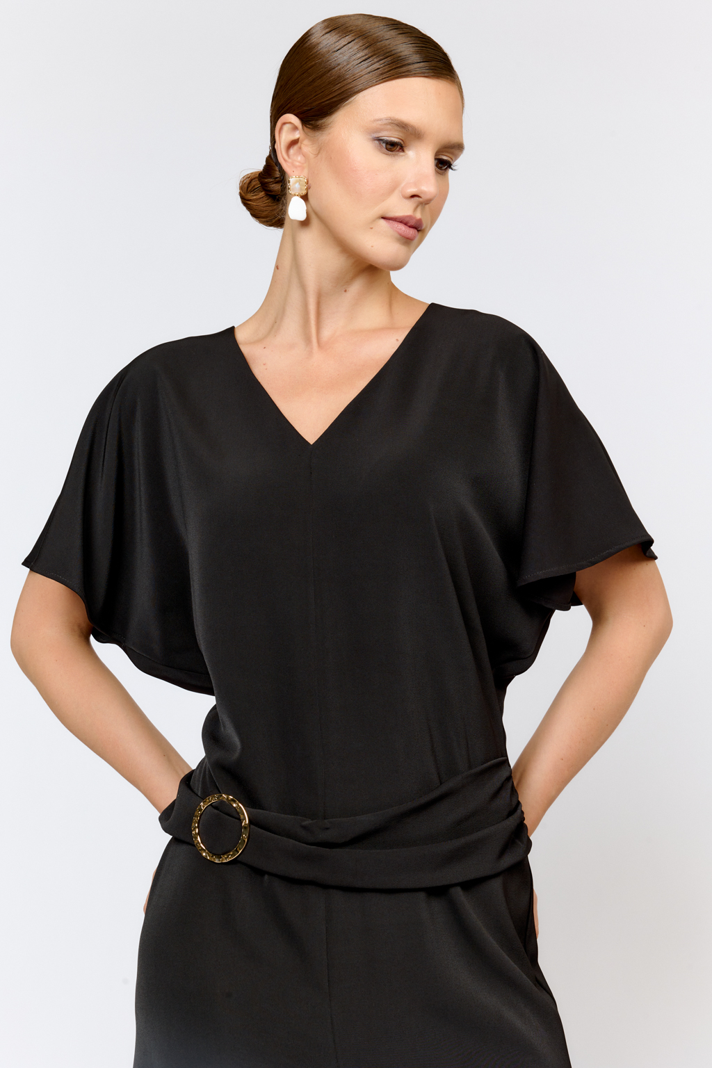 Струящееся платье свободного кроя с цельнокроеными рукавами и открытой горловиной с V-образным вырезом горловины. Модель с декоративной пряжкой на притачном поясе со сборкой по бокам. Выполнено из эластичной плательной ткани. Полиэстер придает ткани устойчивость к сминанию и хорошо держит форму. Что позволяет изделию сохранять опрятный вид в течении дня.  Глубокий черный цвет не тускнеет после стирки. Спандекс добавляет эластичность, обеспечивая идеальную посадку по фигуре. Преимущества ткани: новое современное качество с мягким блеском и благородной фактурой. Ткань легкая, приятна к телу, красиво драпируется при движении. Глубокий черный оттенок придает изделию благородный вид.