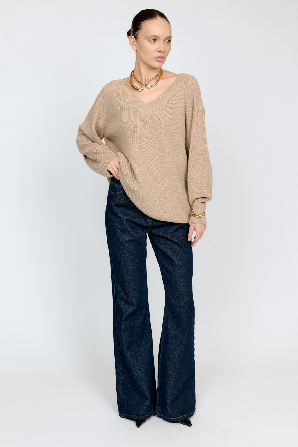 Трикотажный джемпер бежевого цвета свободного силуэта с V-образным вырезом горловины и рукавами реглан из шерстяной смесовой пряжи станет центром комфортных осенних образов.