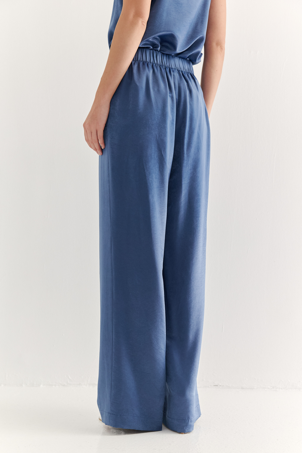 Брюки, широкие и прямые по всей длине, выполнены из струящегося атласа, что является воплощением актуального тренда на мягкий комфорт. Стильный цвет классического денима и фактура ткани, напоминающая мокрый шёлк, определяют ключевое направление в моде: создание атмосферы комфорта, пронизанной заботой и бережным отношением к себе. Брюки оснащены удобными карманами и эластичным поясом, обеспечивающими максимальный комфорт и удобство. Идеальным дополнением к этим брюкам станут топ и жакет в пижамном стиле, позволяющие создать элегантный монохромный образ.