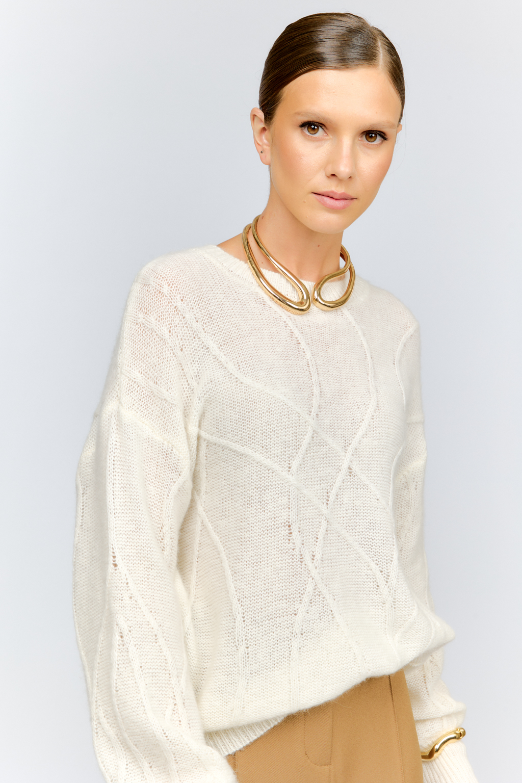 Нежный молочный  джемпер из мягкой шерстяной пряжи с трендовым ажурным дизайном, круглой горловиной, со спущенной линией плеча и длинными рукавами имеет  свободный силуэт оверсайз. Уникальный узор привлекает внимание и придает образу стильный акцент.