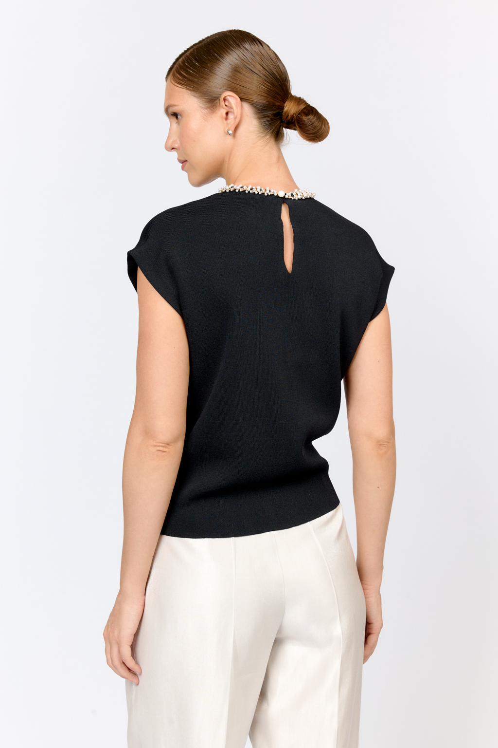 Элегантный топ  с круглой горловиной, декорированной тесьмой. Со спущенным плечом, без рукавов. Свободного силуэта. Изысканная модель из премиального  трикотажа плотной вязки в  молочном цвете. Сбалансированная комбинация вискозы и полиамида  создает комфорт при носке. Материал хорошо держит форму  и не подвержен деформации.  Лаконичный топ с декоративной тесьмой  в универсальном черном цвете  - утонченное решение для вечерних или деловых образов.
