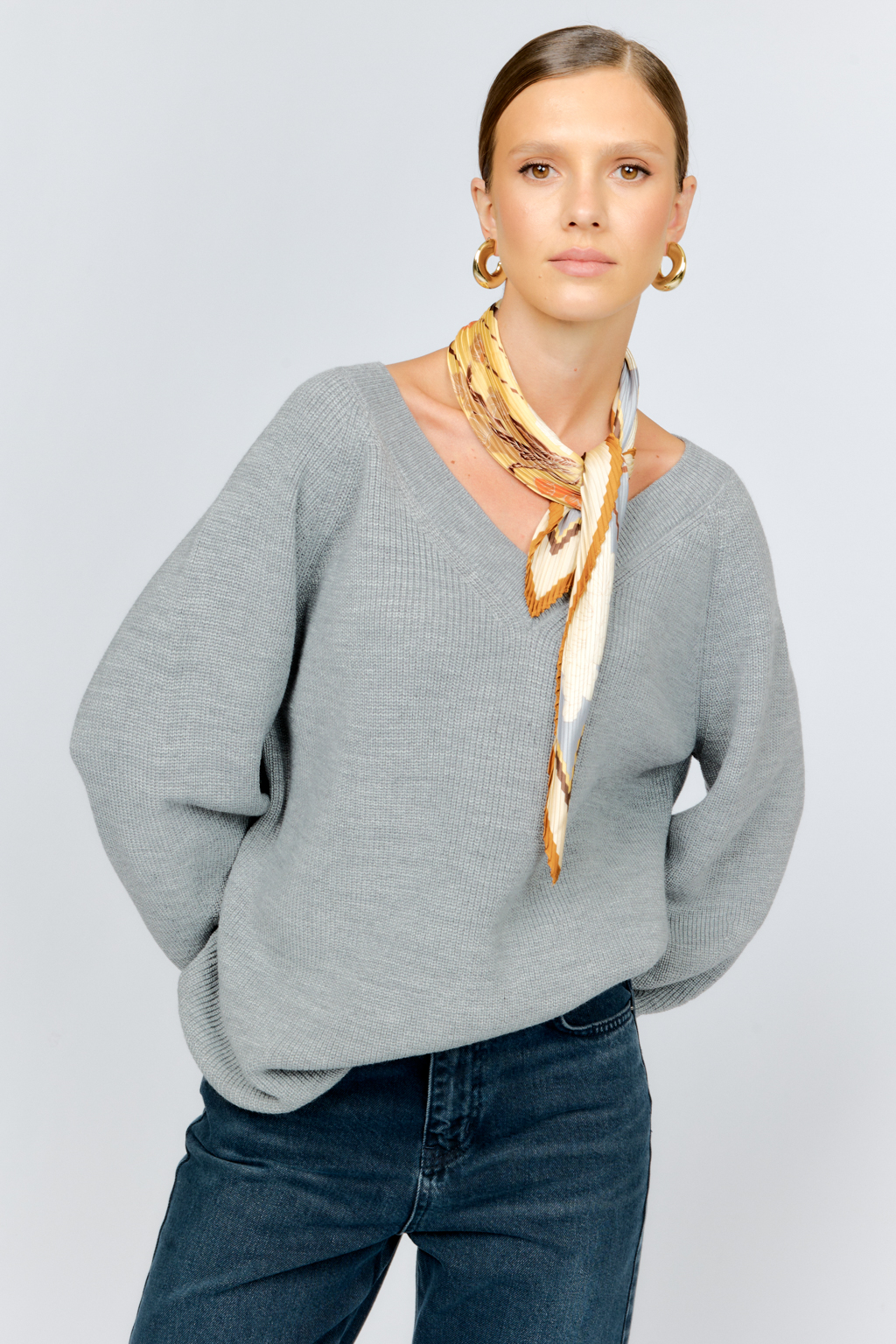 Трикотажный джемпер серого цвета свободного силуэта с V-образным вырезом горловины и рукавами реглан из шерстяной смесовой пряжи станет центром комфортных осенних образов.