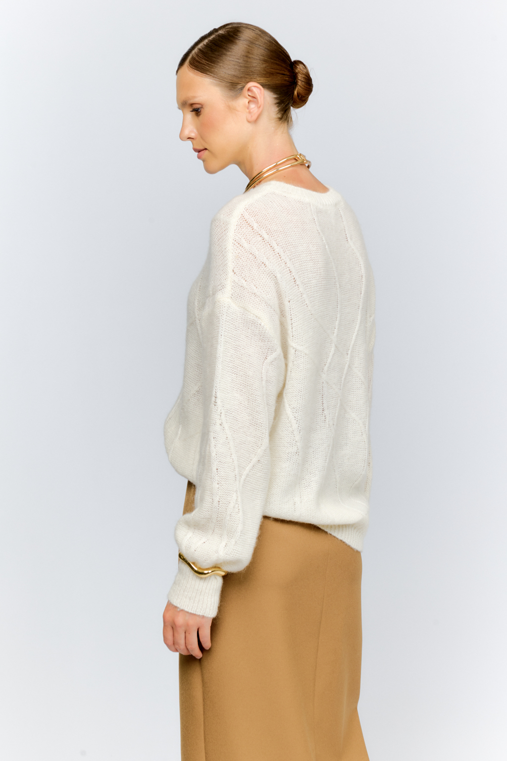 Нежный молочный  джемпер из мягкой шерстяной пряжи с трендовым ажурным дизайном, круглой горловиной, со спущенной линией плеча и длинными рукавами имеет  свободный силуэт оверсайз. Уникальный узор привлекает внимание и придает образу стильный акцент.