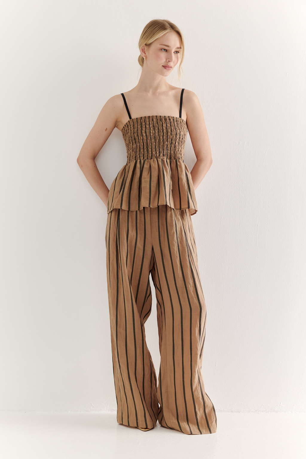 Топ-бандо из эластичных стрейч-нитей, выполненный из платьевой ткани с полской. Состав ткани представляет собой гармоничное сочетание натуральных волокон крапивы и хлопка, обработанных методом растительного окрашивания (natural dye), что обеспечивает экологичность и мягкость материала. Топ состоит из двух основных частей: верхней присборенной бандо-секции и нижней части топа. Поддержка обеспечивается съемными бретелями, которые позволяют варьировать стиль ношения.