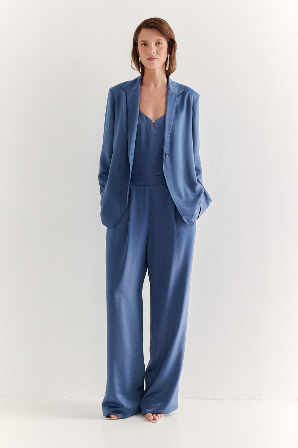 Брюки, широкие и прямые по всей длине, выполнены из струящегося атласа, что является воплощением актуального тренда на мягкий комфорт. Стильный цвет классического денима и фактура ткани, напоминающая мокрый шёлк, определяют ключевое направление в моде: создание атмосферы комфорта, пронизанной заботой и бережным отношением к себе. Брюки оснащены удобными карманами и эластичным поясом, обеспечивающими максимальный комфорт и удобство. Идеальным дополнением к этим брюкам станут топ и жакет в пижамном стиле, позволяющие создать элегантный монохромный образ.