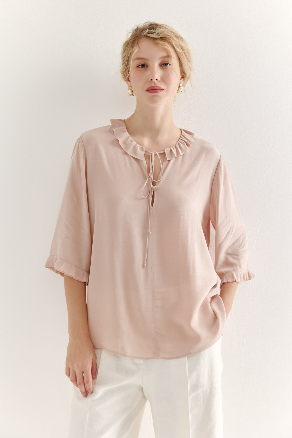 Эта романтичная блуза выполнена из вискозного крепа в нежном пудрово-розовом оттенке. Горловина и рукава украшены изящными рюшами, добавляющими образу легкости и утонченности. Оригинальный разрез спереди кокетливо завязывается на тонкий шнур-рулик и фиксируется воздушной петлей на пуговицу. Прямой силуэт и рукава длиной одна вторая обеспечивают комфорт и свободу движений. Эта блуза — идеальный выбор для создания непринужденных, но элегантных городских образов.