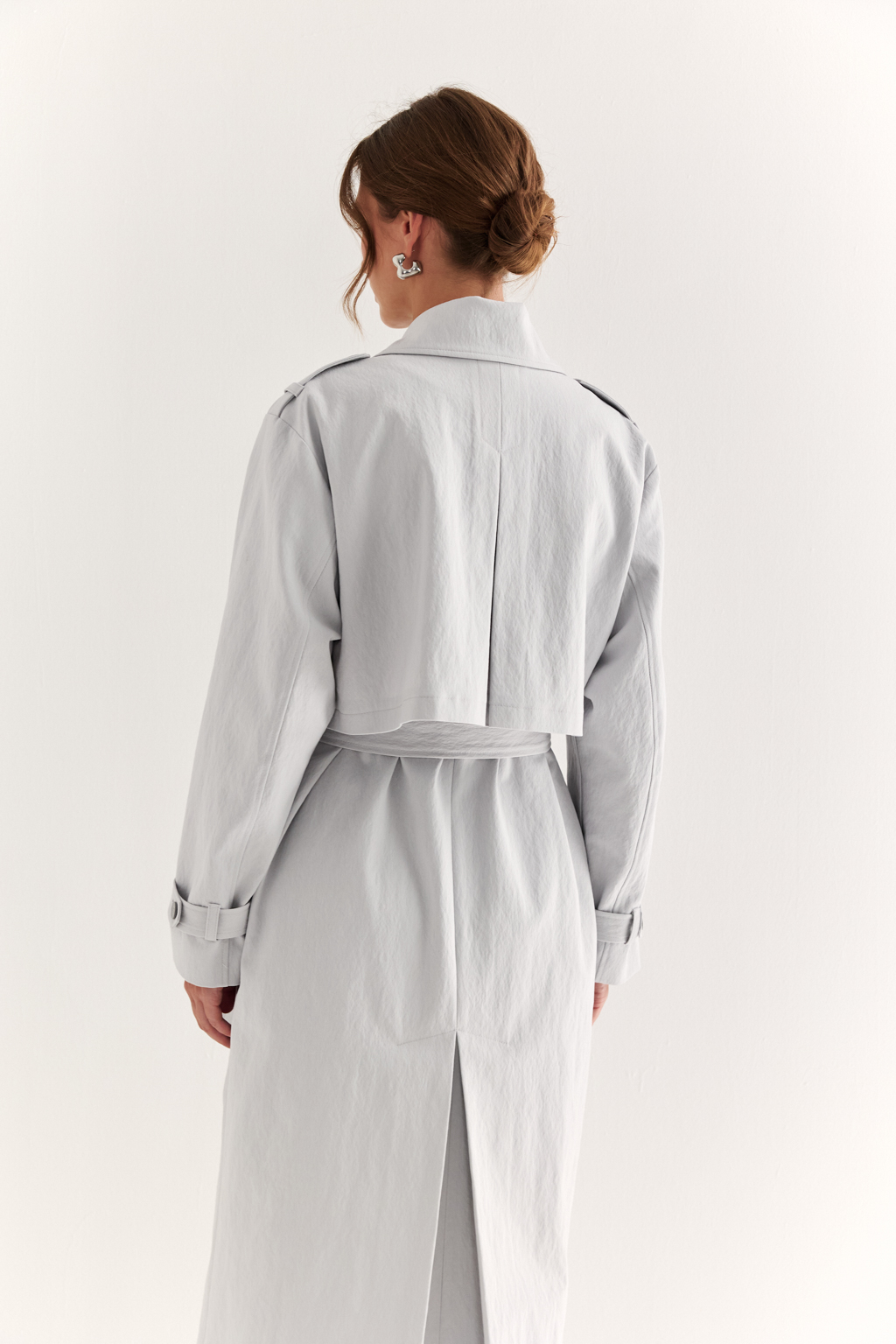 Плащ двубортный прямого силуэта длиной макси с расширенной линией плеча и отлётными кокетками по полочке и спинке. Приталивается завязывающимся поясом.